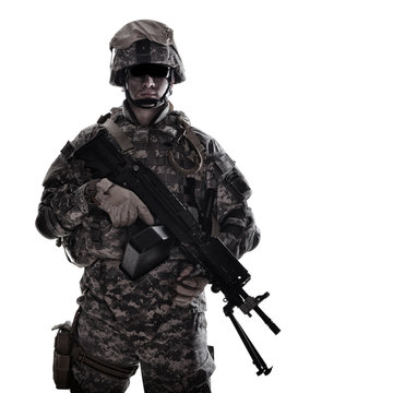 Low key studio portrait of US Armed Forces soldier in protective camouflage, helmet and tactical sunglasses holding light machine gun and looking in camera desaturated, isolated on white background