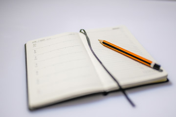 A personal organizer with open a pencil on it. Macro of pencil and notebook on white background out of focus. Details on focus of a wooden pen orange and black on an agenda