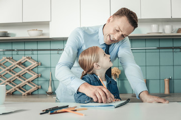 Obraz premium Child upbringing. Happy male person keeping smile on face and bowing head while studying with his daughter