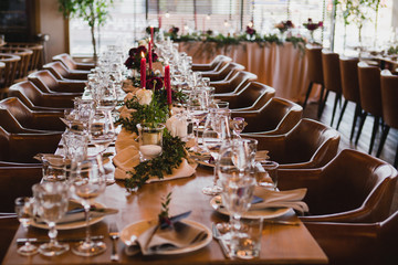Coziness and style. Modern event design. Table setting at wedding reception. Floral compositions with beautiful ranunculus flowers and greenery, candles, laying and plates on decorated table.
