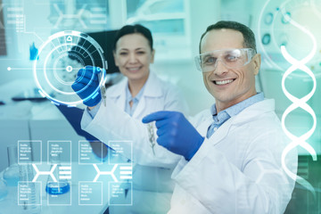 Happy scientists. Emotional clever scientist holding samples in tin test tubes and smiling while his cheerful colleague sitting near
