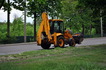 Bright orange excavator tractor on the road along park, spring in Kharkiv, Ukraine
