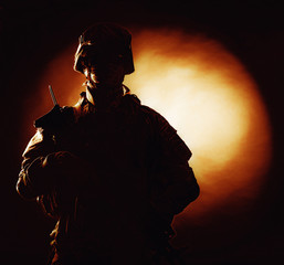 Silhouette photo of army soldier, modern combatant, military conflict participant standing in combat uniform with fiery spot on black background. Fire of war, ashes of battle, nuclear fire concept
