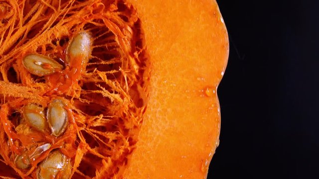 Macro shot of raw pumpkin with seeds rotating on black background in 4K with free place for text. Sweet tasty vegetable before backing on autumn parties like Thanksgiving, Halloween.
