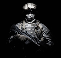 United States Armed Forces soldier in battledress with black glasses and mask on face, armed squad automatic weapon emerges from darkness. Military threat, secret stealth mission, hybrid war combatant