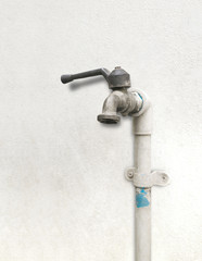 Fototapeta na wymiar Old faucet isolated on white concrete wall. degraded