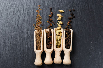 Various of spices and herbs in wooden spoons. Flat lay of spices on black stone