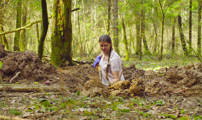 Woman ecologist in the forest digging a soil slit with the shovel.