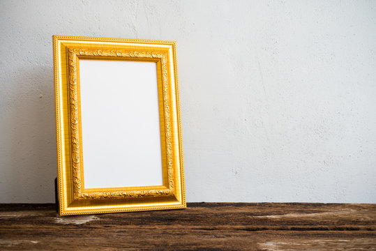 Golden vintage photo frame on old wooden table over white wall background