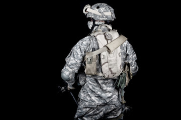 Back view of modern military forces infantry, US marine armed with rifle in digital camouflage combat uniform, protected helmet and body armour with hydration pack on back isolated on black background