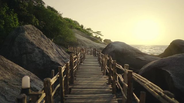POV Moving Dolly Shot of a Wooden Path on the Shore Between Big Rocks and with Ocean in View.