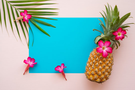 Flat lay of pineapple, flowers, palm leaf on pink and blue background with copy space, tropical summer holiday vacation, wedding invitation party concept