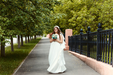 beautiful cheerful bride in a white dress and veil with a bouquet in her hands looking at the camera in the Park in full length summer