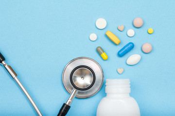 White bottle with different pills, capsules and phonendoscope on blue background