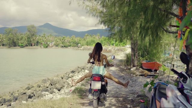 Beautiful Asian Woman on a Scooter Starts Driving on a Rocky Road near the Sea. Shot on RED Epic 4K UHD Camera.