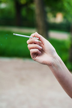 Cigarette in a female hand on a green background. Vertical photo.