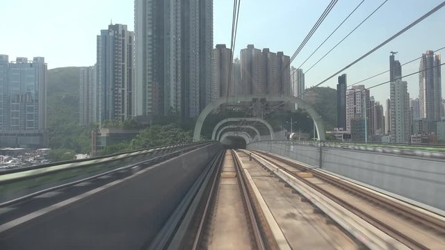 Train moves along metro or subway railroad half-open tunnel and passes by Hong Kong city buildings and skyscrapers. Electric rapid public transport, urban mass transit railway system or MTR.