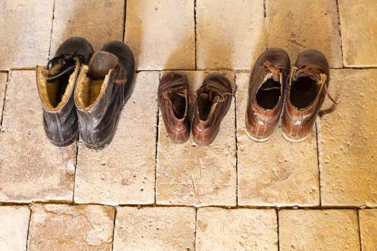 Top view of three pairs of old worn leather shoes in a line on beige stone floor.