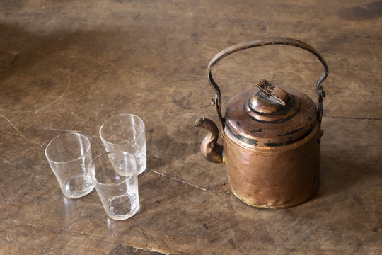 Still life with a beautiful worn retro style copper tea kettle with three empty glasses on a massive wooden table.