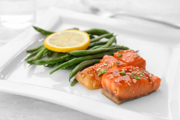 Fish fillet served with lemon slice and green beans on plate, closeup