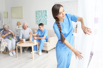 Young woman in uniform opening curtains indoors