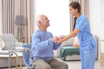 Senior man and young caregiver holding hands indoors