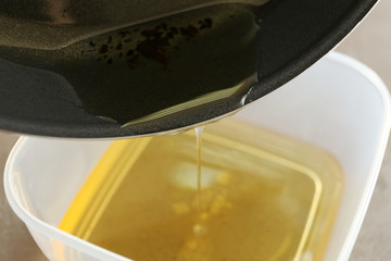 Pouring used cooking oil from frying pan into plastic container, closeup