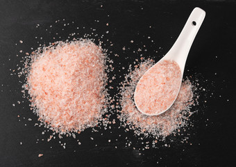 Himalayan pink salt in ceramic spoon on black stone background