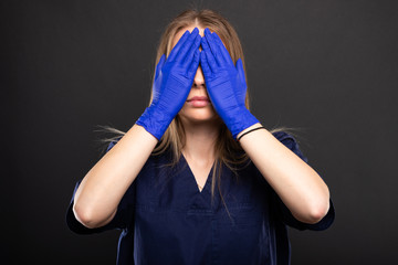Female doctor wearing scrubs covering eyes like blind concept.