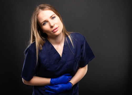 Beautiful female doctor wearing scrubs making stomach ache gesture.