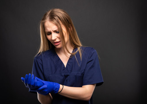 Beautiful female doctor wearing scrubs making wrist pain gesture.