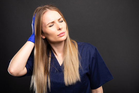 Beautiful female dentist wearing scrubs making headache gesture.