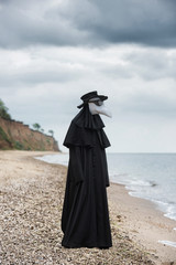 Plague doctor in seaside. Outdoor portrait with dramatic sky in background.