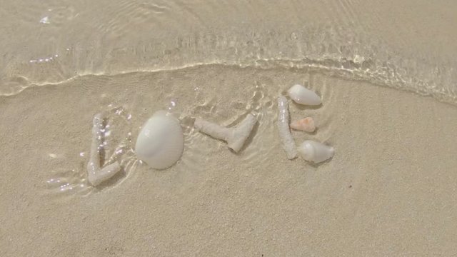 Gentle Sea Waves Covering The Word Love Created With Shells And Corals On The Beach.