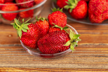 Ripe red organic strawberries in a glass bowl against brown wooden background.