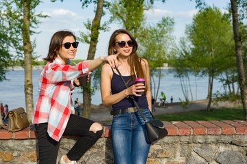 Outdoors portrait of female friends drinking coffee and having fun. Background nature, park, river. Urban lifestyle and friendship concept.