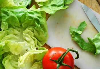 Листья зеленого салата, помидор, деревянный стол