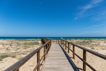 Fototapeta na wymiar Wooden bridge landscape at the beach ending in turquoise blue sea