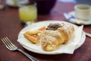 Close-up of a chocolate croissant with icing sugar and slice of cake on a plate. Sweet brakfast