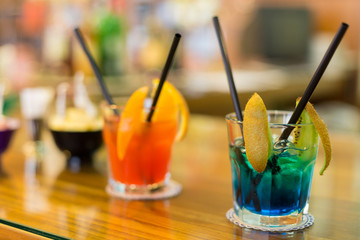  Orange and blue cocktails on the bar counter. Close-up of a blue cocktail with kiwi slices and two black straws