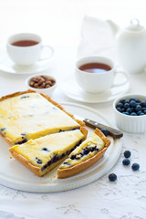 Tea time. Homemade blueberry cheesecake, cups of tea, nuts and berry on white table cloth