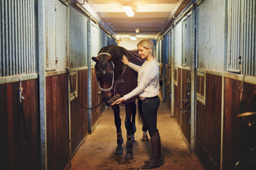 Smiling woman preparing her horse in stables before a ride