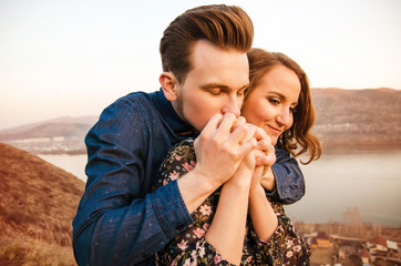 Guy kisses the hands of his beloved girl in the background of the hills and the river.