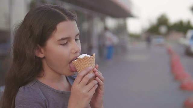 little girl eating ice cream goes down the street in the city next to the supermarket with a soft toy motion slow motion video. girl and lifestyle ice cream urban eat concept