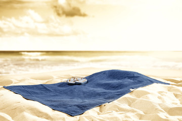 Blue towel and flip-flops on hot summer beach sand with copy space. Products placement and seascape...