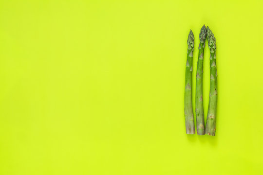 Asparagus sprouts on bright green surface.