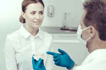 How informative. Diligent young patient listening attentively to her experienced doctor with the model of jaws in his hands