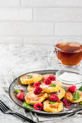 Healthy summer breakfast, cheese pancakes with raspberry, powdered sugar and mint, grey concrete background copy space