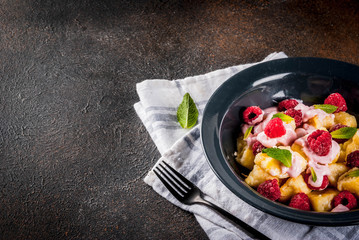 Ukrainian, Russian food, lazy vareniki; Curd or cheese gnocchi with fresh raw raspberries, cream and mint, on a dark concrete background, copy space top view