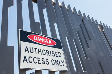 Warning sign against unauthorised access on a high steel fence.